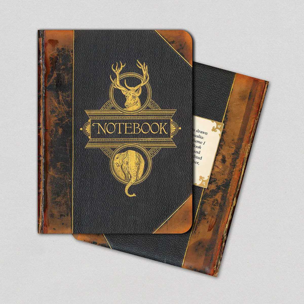 Two Animals on Brown vintage book cover notebooks stacked at an angle showing dark charcoal textured cover with gold foil stag and elephant crest and aged brown spine on gray background