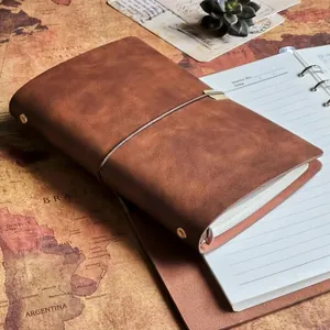 Vintage distressed brown PU leather refillable journal with elastic strap closure, closed on antique map background with open white notebook beside it