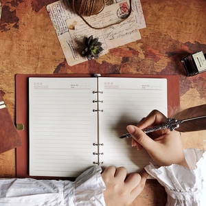 Vintage PU leather journal open to lined pages spread, hand writing with feather quill pen, antique map and compass background