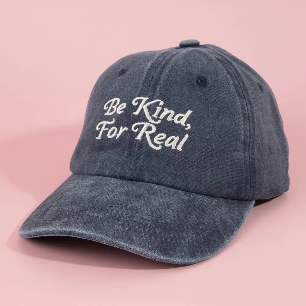 Washed navy baseball cap with Be Kind For Real cream embroidery on pink background