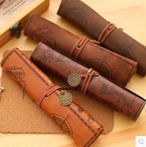Four vintage roll-up pencil cases in dark brown and tan faux leather with embossed nautical treasure map and compass print, cord tie closure and coin pendant, displayed rolled and unrolled on wooden surface