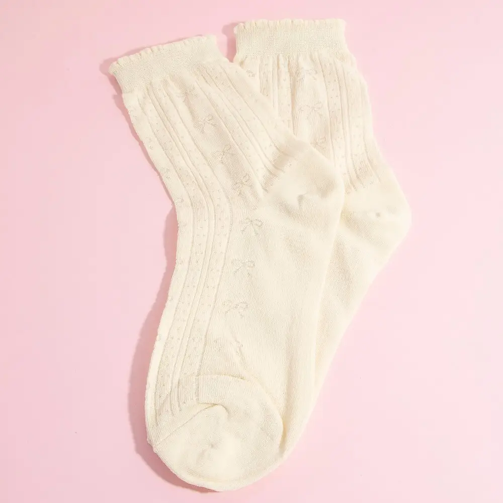 Cream ribbed crew socks with subtle bow accents flat lay on pink background